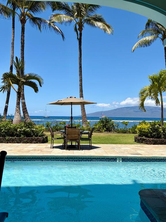 a pool with palm trees and a table and umbrella at Compass Blue Lahaina in Lahaina