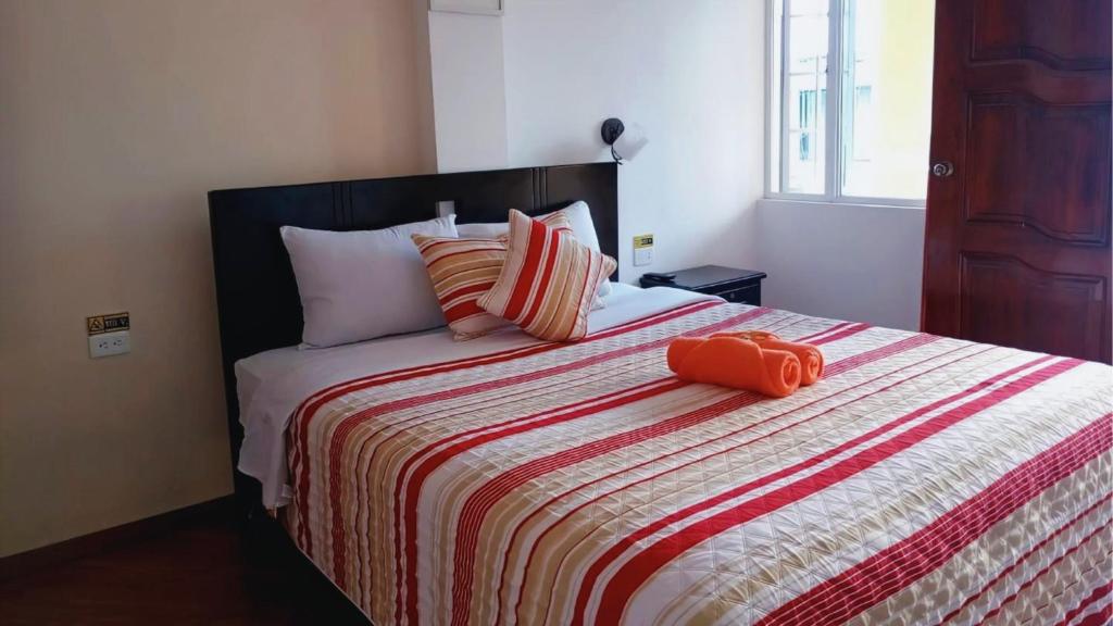a bed with an orange pillow on top of it at Hostal Mariscal Sucre in Tababela