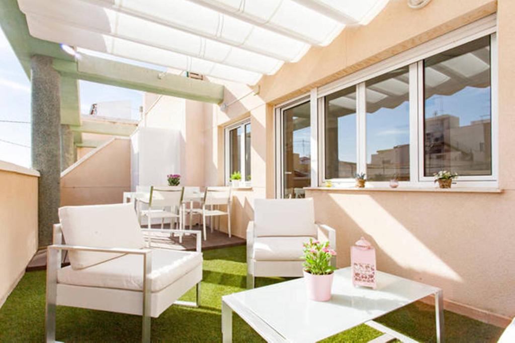 un patio con sillas blancas, mesas y ventanas en Lovely Loft Auditorio, en Alicante
