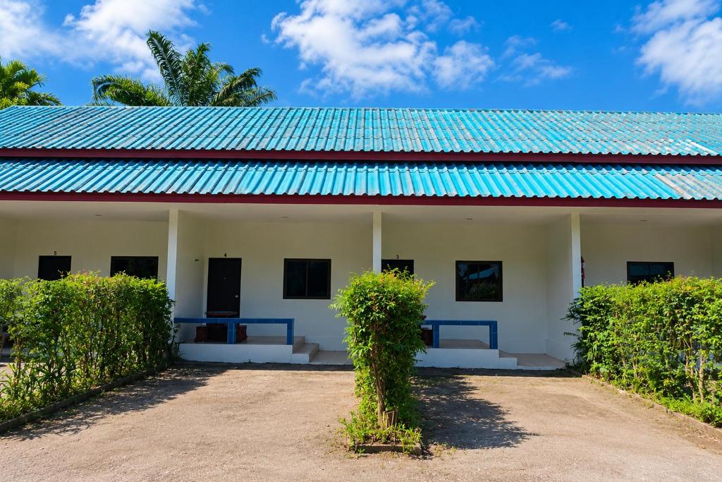 a white building with a blue roof and bushes at 169 Home Resort in Ban Huai Khram