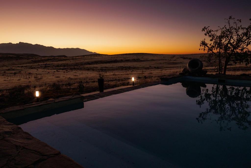 a swimming pool with the sunset in the desert at 3 ALOES GUESTHOUSE in Uis