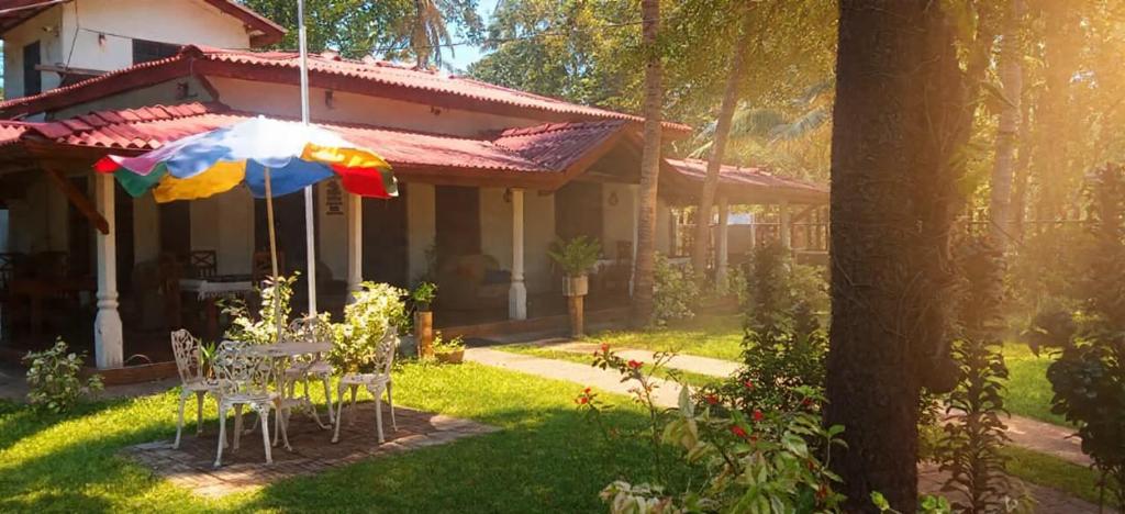 a house with a table and an umbrella in the yard at Rio Lake Hotel Sigiriya in Habarana