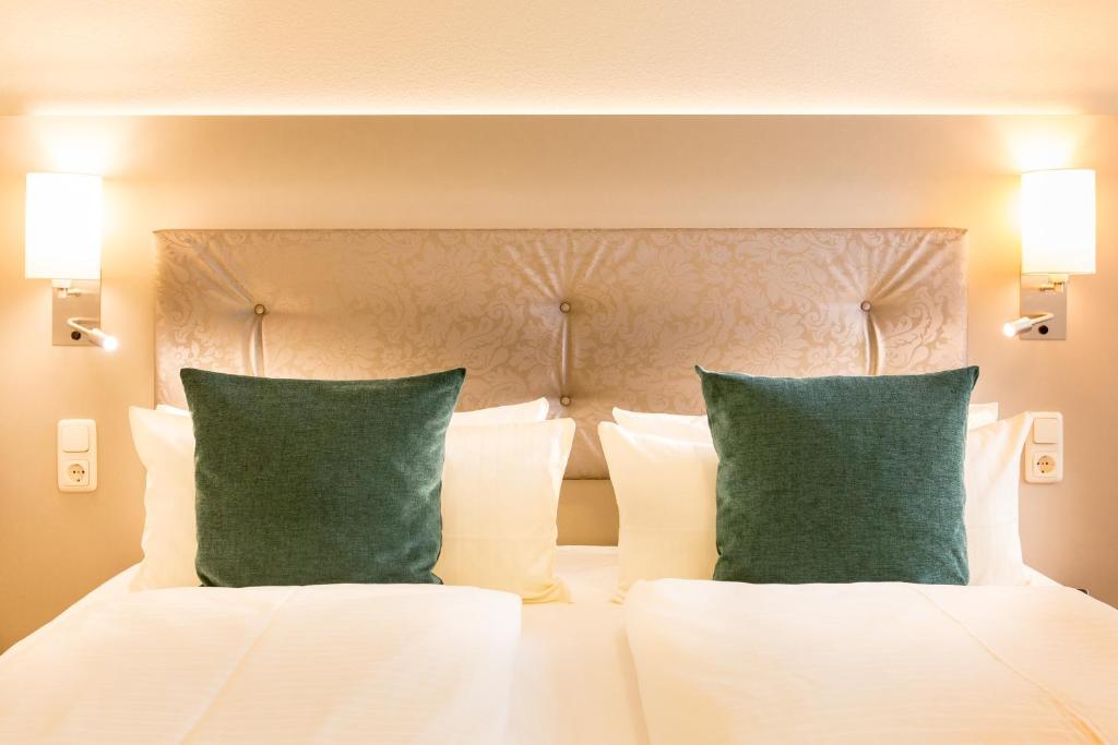 Hermes Hotel Oldenburg في أولدنبورغ: غرفة نوم بسرير ابيض مع وسادتين خضراء