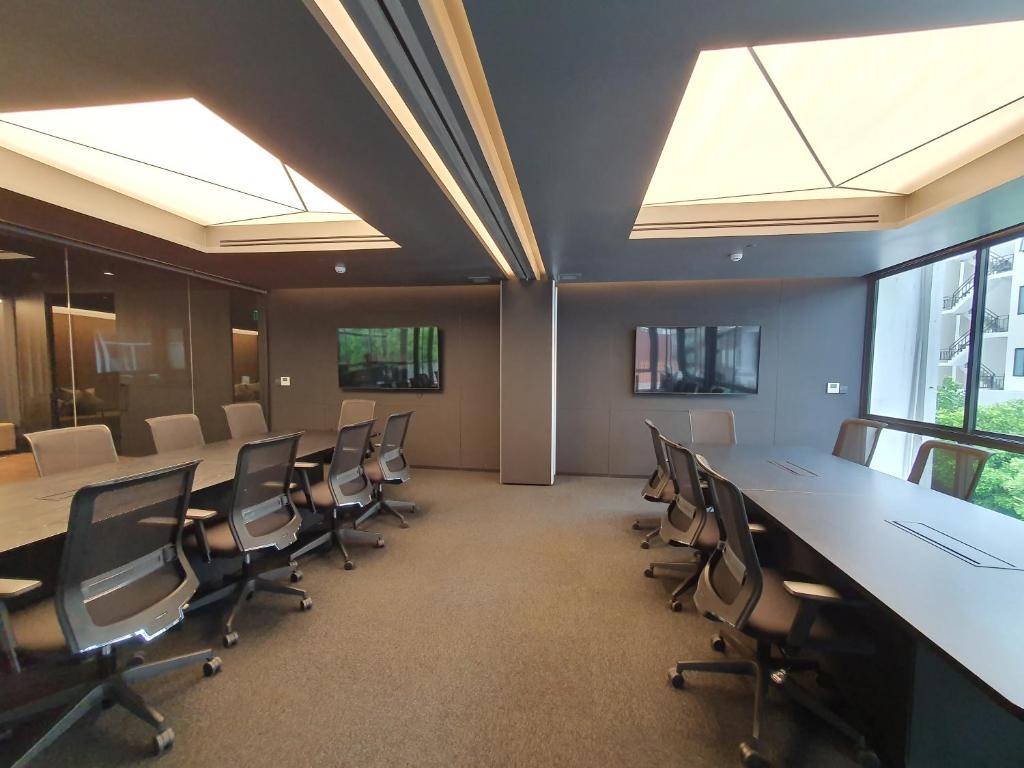 A bright meeting room with long tables, rolling office chairs, and windows on one side.
