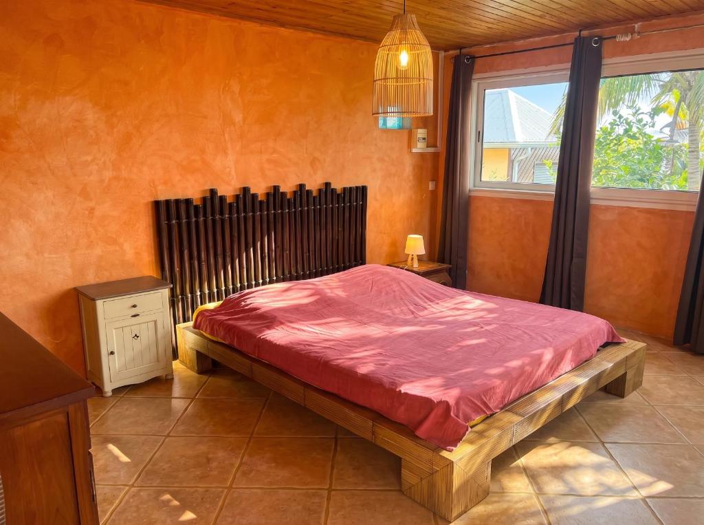 a bedroom with a bed with a red comforter and a window at Bungalow cosy à Saint-Leu, vue sur la mer. in Saint-Leu