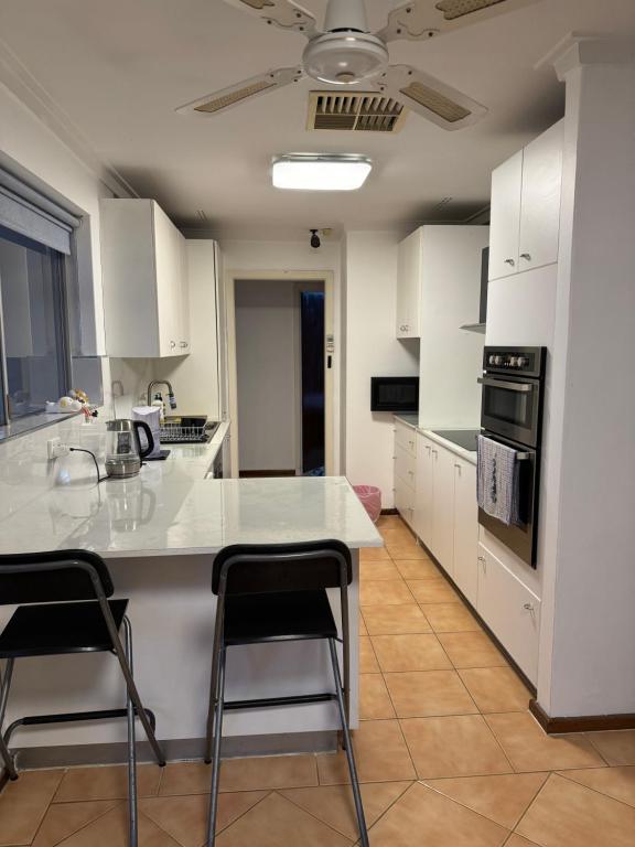 a kitchen with white cabinets and a counter with stools at Nice quite stay in Perth