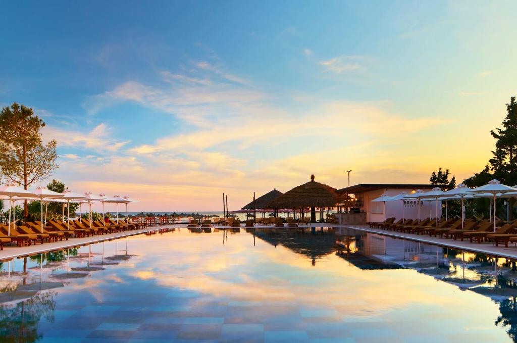 a swimming pool with chairs and buildings and a sunset at SOL by Meliá Tropikal Durres in Durrës