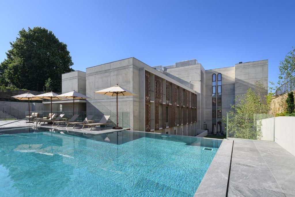 a swimming pool with chairs and umbrellas in front of a building at INNSiDE by Meliá Braga Centro in Braga