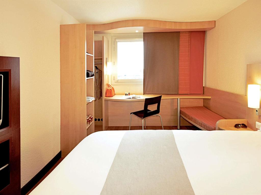 A compact room with a desk, chair, bench seat and bed.