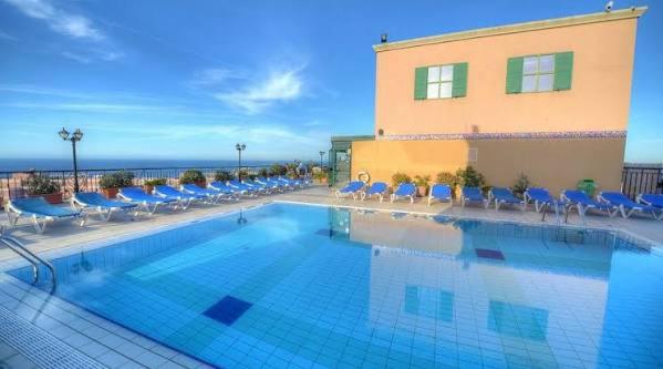 a large swimming pool with blue chairs and a building at Vivaldi Hotel in St. Julianʼs