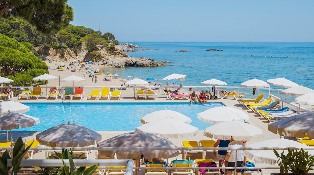 a swimming pool with umbrellas and people on a beach at htop Caleta Palace - Bliss in Platja d'Aro