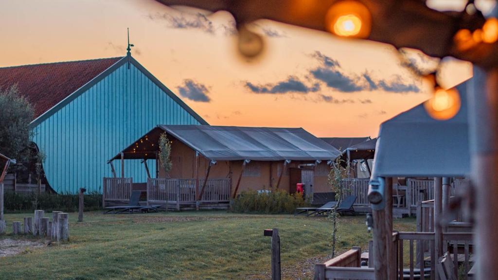 a large barn with a blue building in the background at Dutchen Erfgoedpark De Hoop Glamping, Appartementen & Cottages in Uitgeest