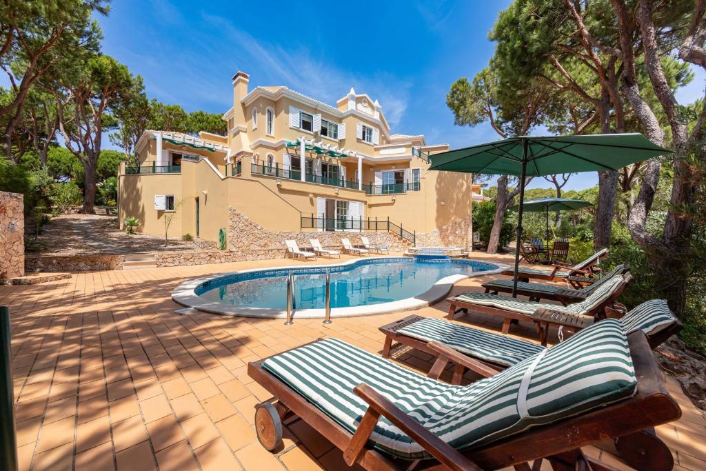 a house with a swimming pool with chairs and an umbrella at Villa Praia Verde - Beach & Nature in Praia Verde