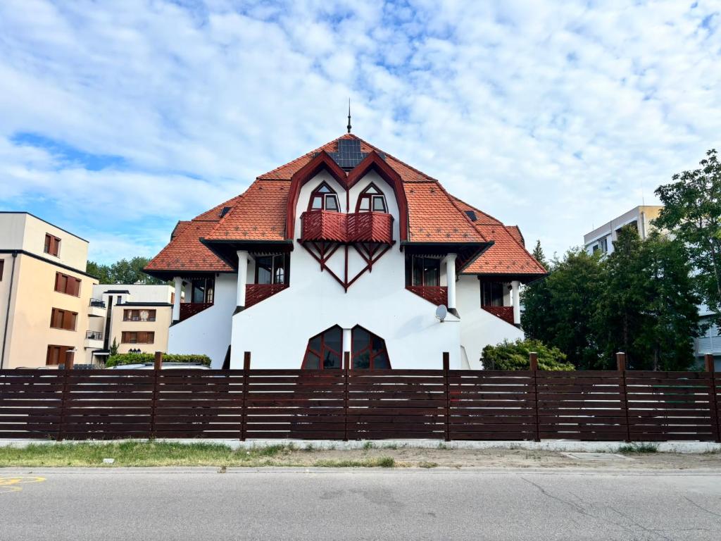 a white house with a red roof behind a wooden fence at Grantek Üdülőház in Balatonlelle