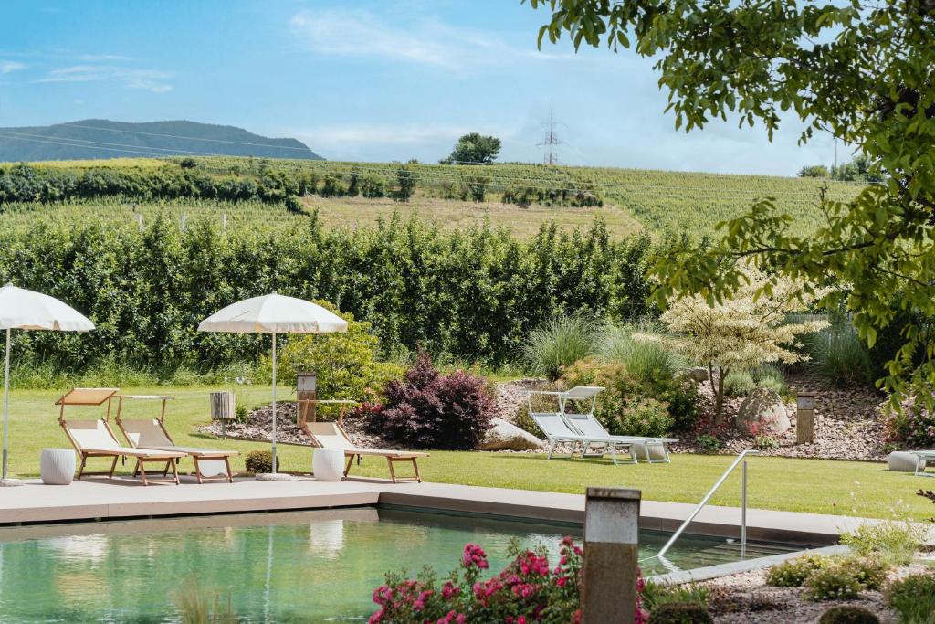 a pool in a garden with chairs and umbrellas at Hotel Girlanerhof in Appiano sulla Strada del Vino