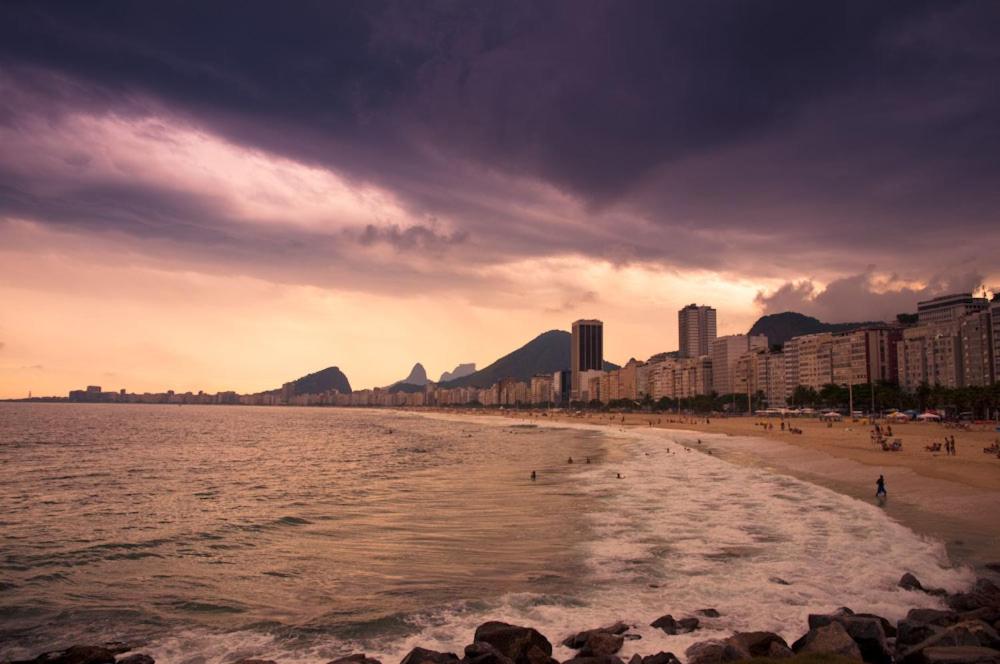 een strand met mensen en gebouwen en de oceaan bij Mar da Babilônia Hostel in Rio de Janeiro