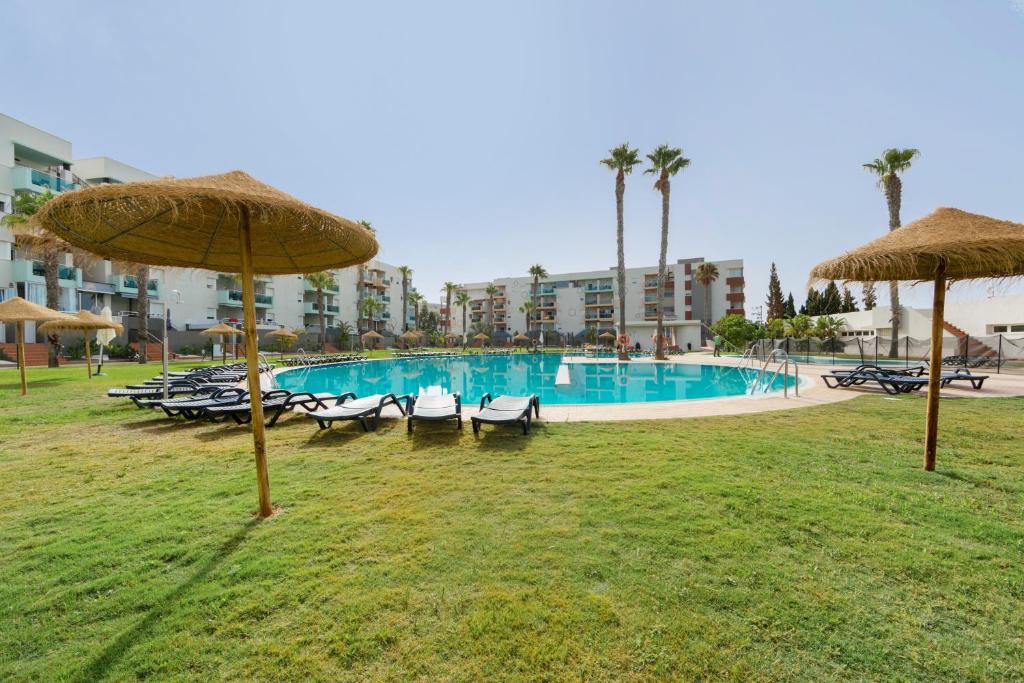 a swimming pool with chairs and umbrellas in a park at Apartamento de lujo Almerimar in Almerimar