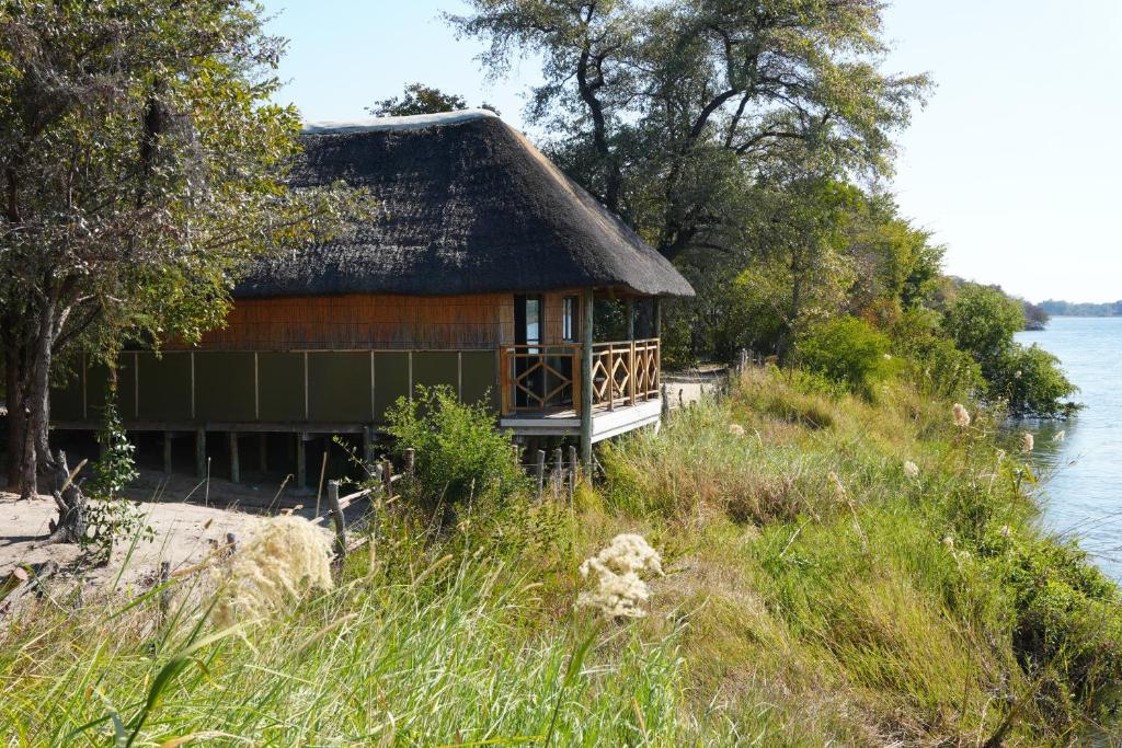 a house with a thatched roof next to the water at Emms Cubango Ecological Camp in Divundu