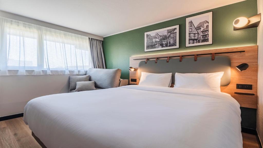 a bedroom with a large white bed and a green wall at Campanile NATURE - Colmar Parc des Exposition in Colmar