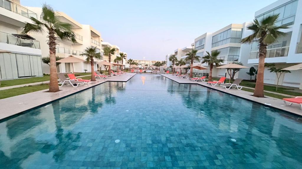 a large swimming pool with chairs and palm trees at Pool View Apartment Gated Residence in Sidi Rahal