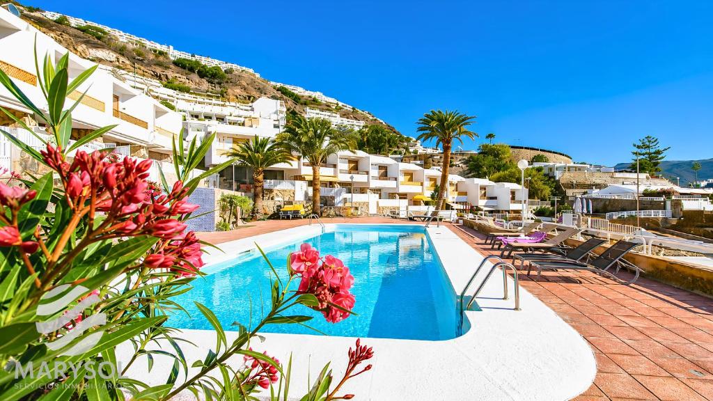 a resort swimming pool with red flowers and buildings at Apartamentos Panamá in Puerto Rico de Gran Canaria