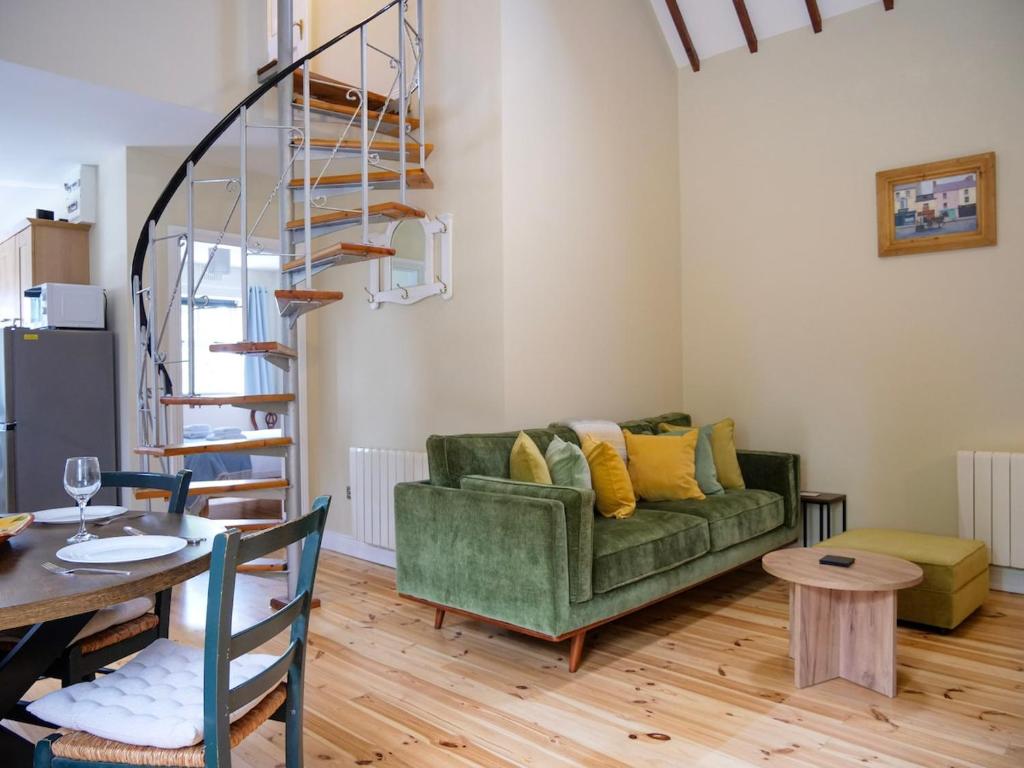 a living room with a green couch and a spiral staircase at Central Dingle Cottage in Dingle