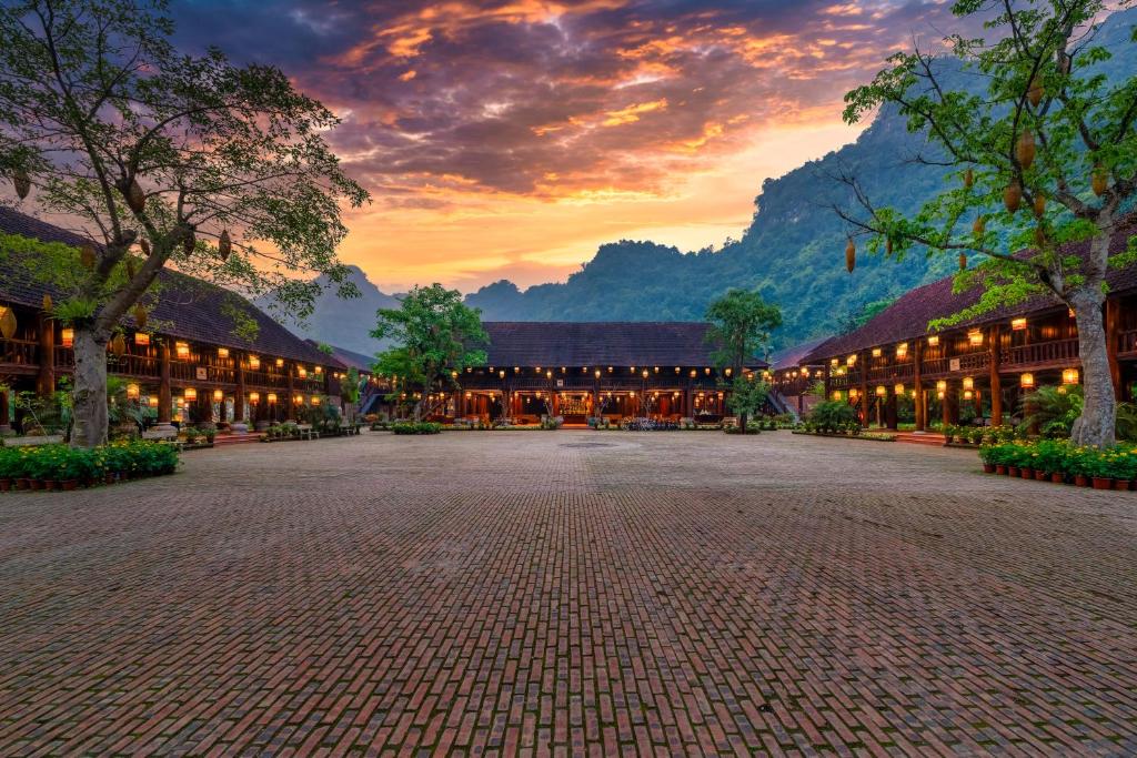 a building with a courtyard with a sunset in the background at Ui Valley Resort in Ninh Binh