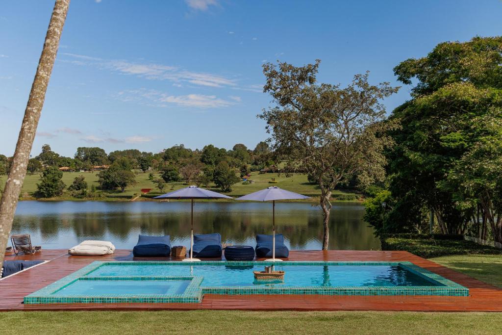 a swimming pool with chairs and umbrellas next to a lake at Casa a jabuticabeira in Avaré