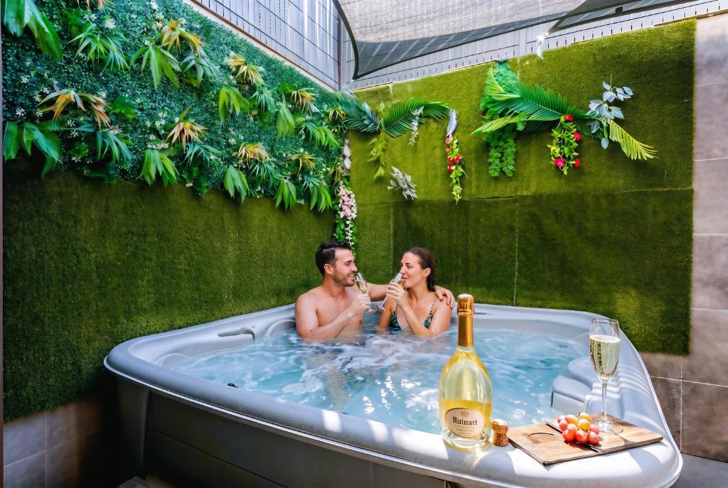 a man and woman in a bath tub with a bottle of wine at Jacuzzi 38C Sauna Privé - Climatisation in Furdenheim