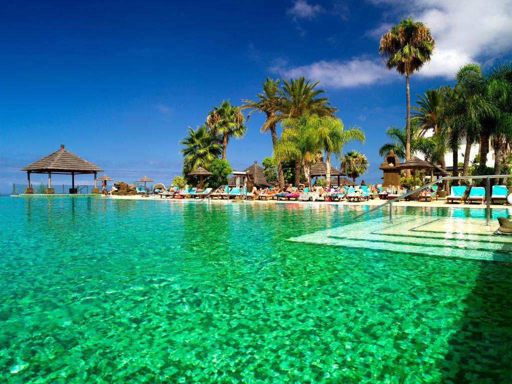 a swimming pool with turquoise water and palm trees at Regency Country Club, Apartments Suites in Playa de las Americas