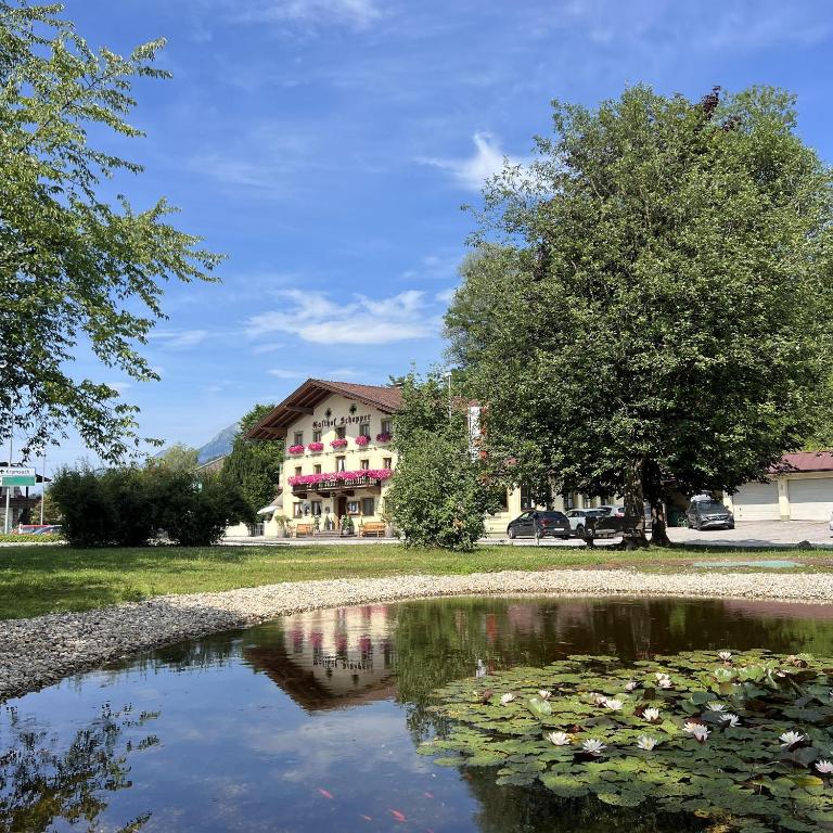 a pond in front of a building with a tree at Gasthof Schopper in Breitenbach am Inn