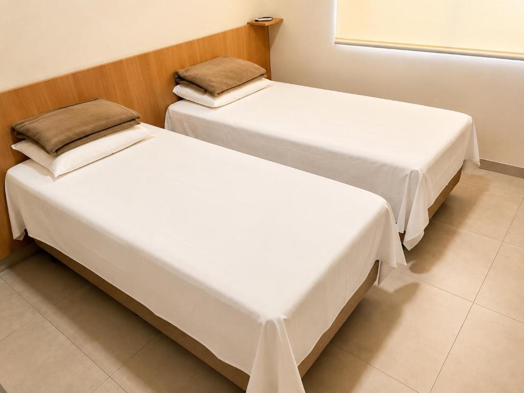 two beds in a room with white sheets and a window at Vêneto Flat Residence (AP-13) in Primavera do Leste