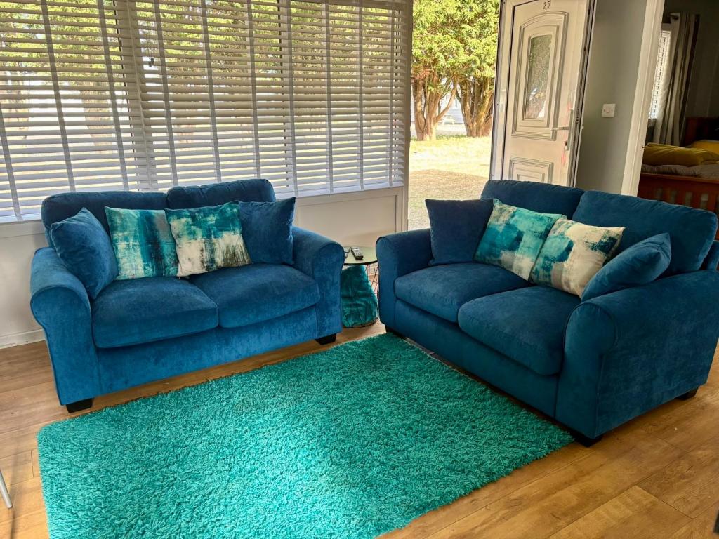 a living room with two blue couches and a green rug at Seashells - Chalet 25 in Greatstone