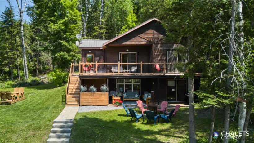 a log home with a deck and chairs in the yard at Le Rustique Moderne Detente - Lake Access in Pohénégamook