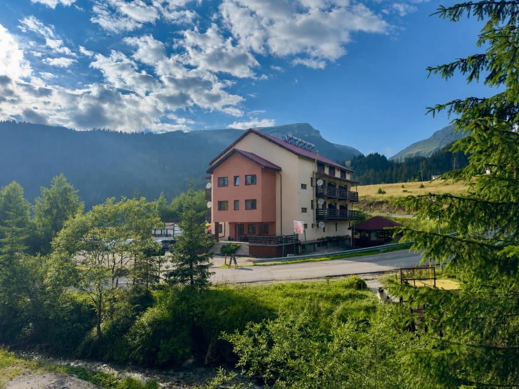 a building on a hill with mountains in the background at Pensiunea Turistică Octavian in Moroeni