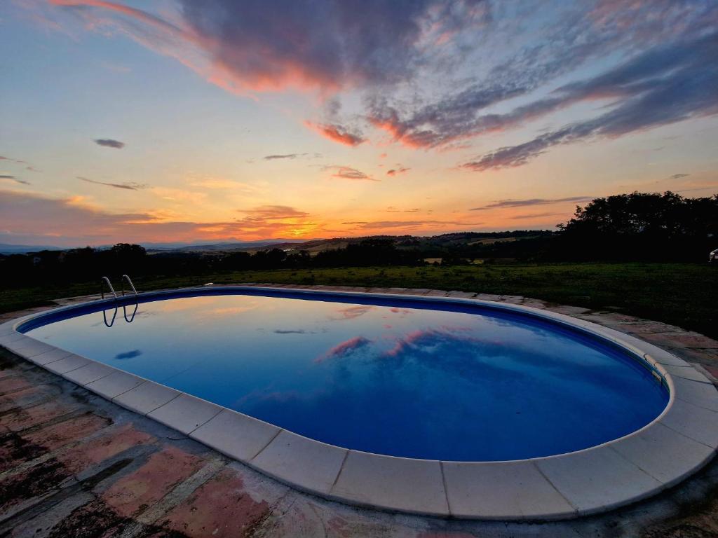 ein großer blauer Pool mit einem Sonnenuntergang im Hintergrund in der Unterkunft alumbia in Petriolo