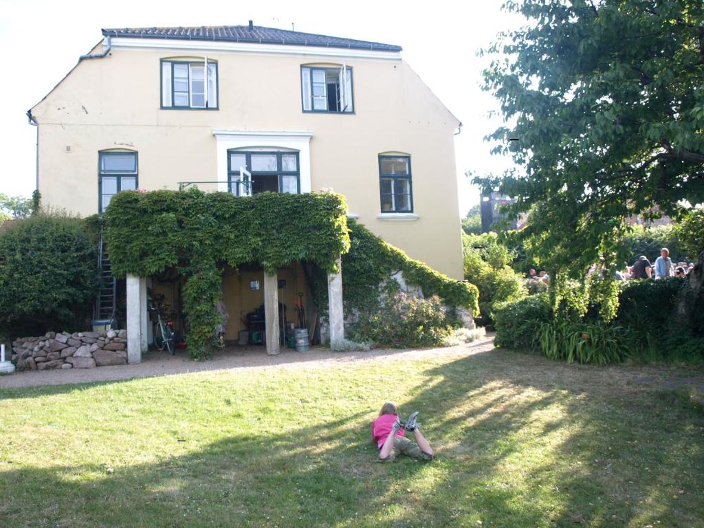a little girl sitting in the grass in front of a house at Danchelshus in Allinge