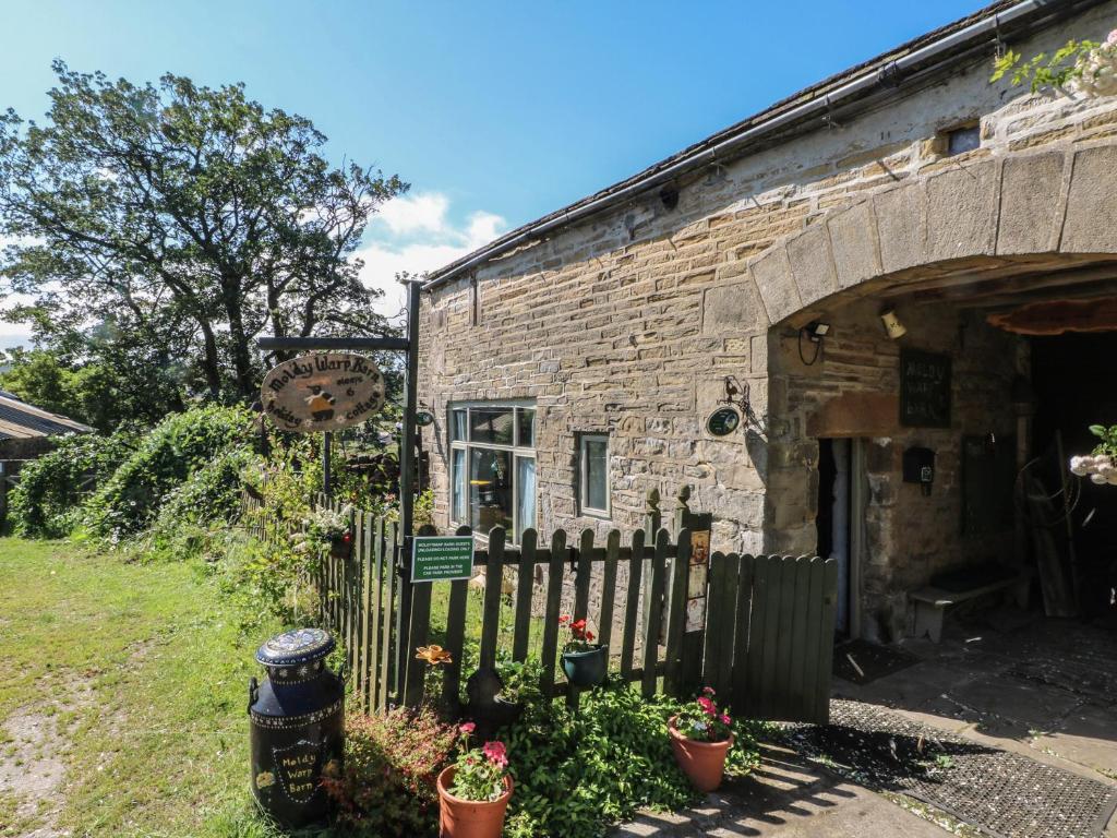 an old stone building with a fence and flowers at Moldy Warp Barn in Keighley