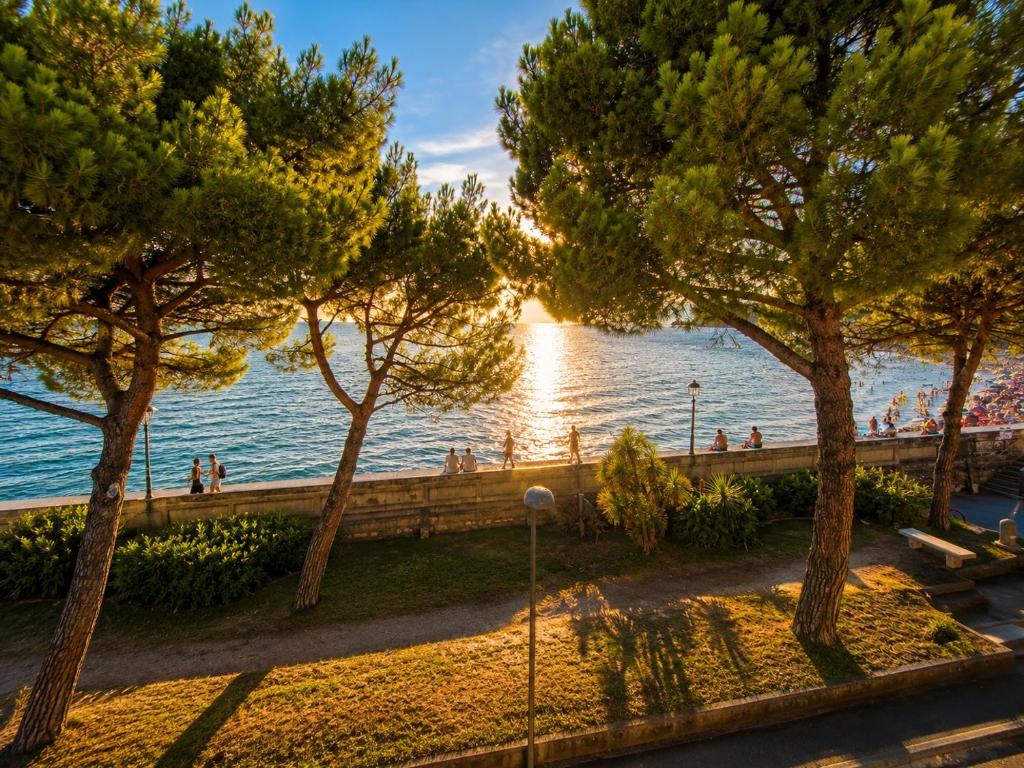 a group of people walking on a sidewalk next to the water at BeachfrontGrado Seaview Apartment Costa Azzurra in Grado
