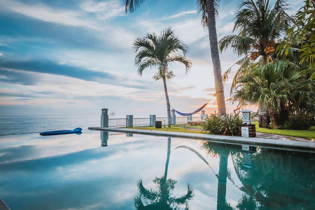 a swimming pool with palm trees and the ocean at Villa Seaview- tranquil 3BR, beachfront, private pool in Bukti