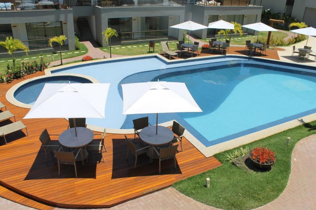 uma grande piscina com mesas e guarda-sóis brancos em Condomínio Solaris Imbassai em Imbassaí