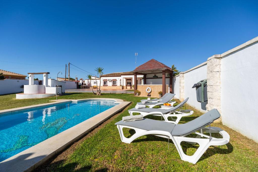 a row of lounge chairs next to a swimming pool at VillaHaba BarrosaHome in Novo Sancti Petri