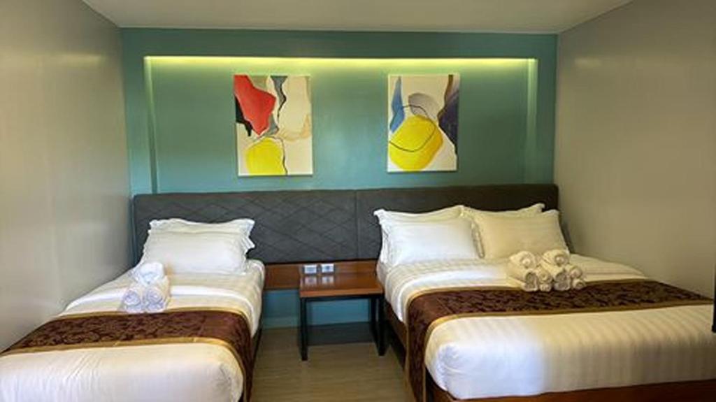 two beds in a hotel room with paintings on the wall at ECL Travellers Inn in Nabas