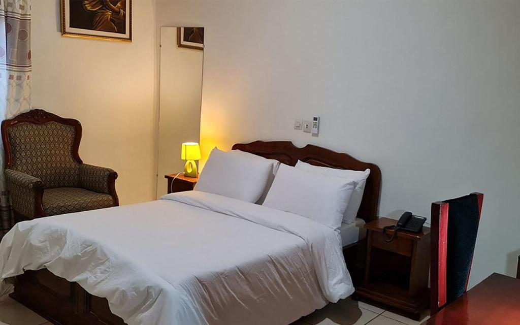 a bedroom with a bed with white sheets and a chair at Hôtel Cauris d'Or de Bouaké in Bouaké