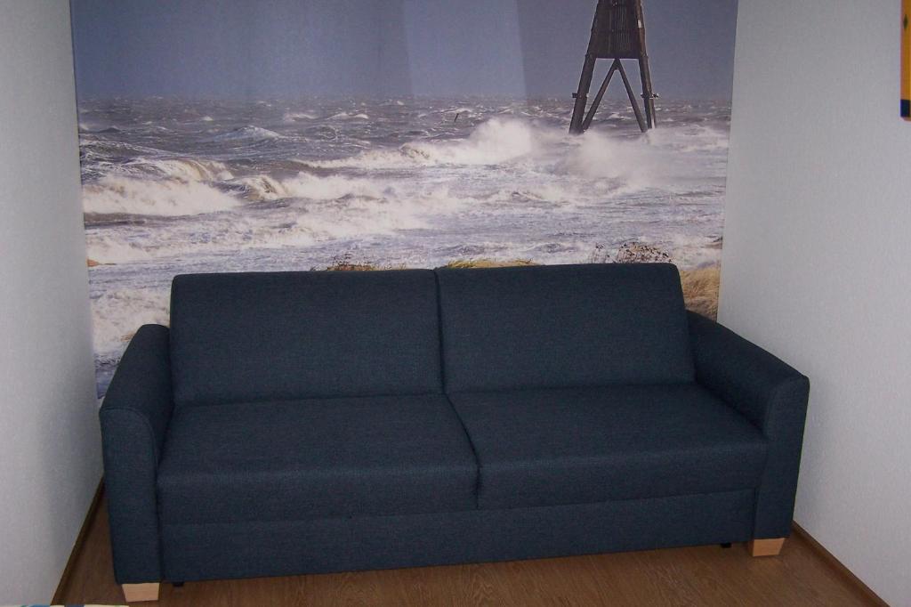 un sofá azul en una habitación con una pintura del océano en Marina 68/70, en Cuxhaven