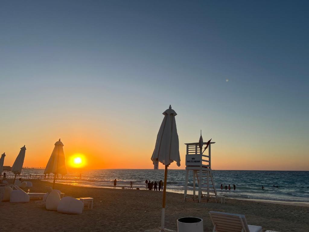 a beach with umbrellas and a lifeguard tower at sunset at Mountain View Chalet in Ras El Hekma ماونتن ڤيو رأس الحكمة in Ras Elhekma