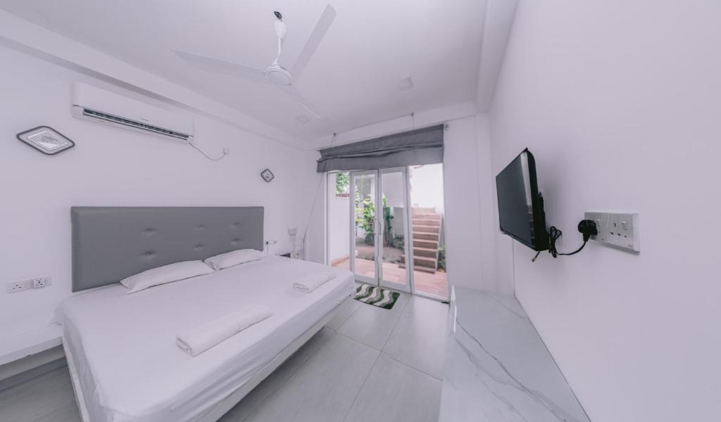 a white bedroom with a bed and a tv at Vega Haven in Matara