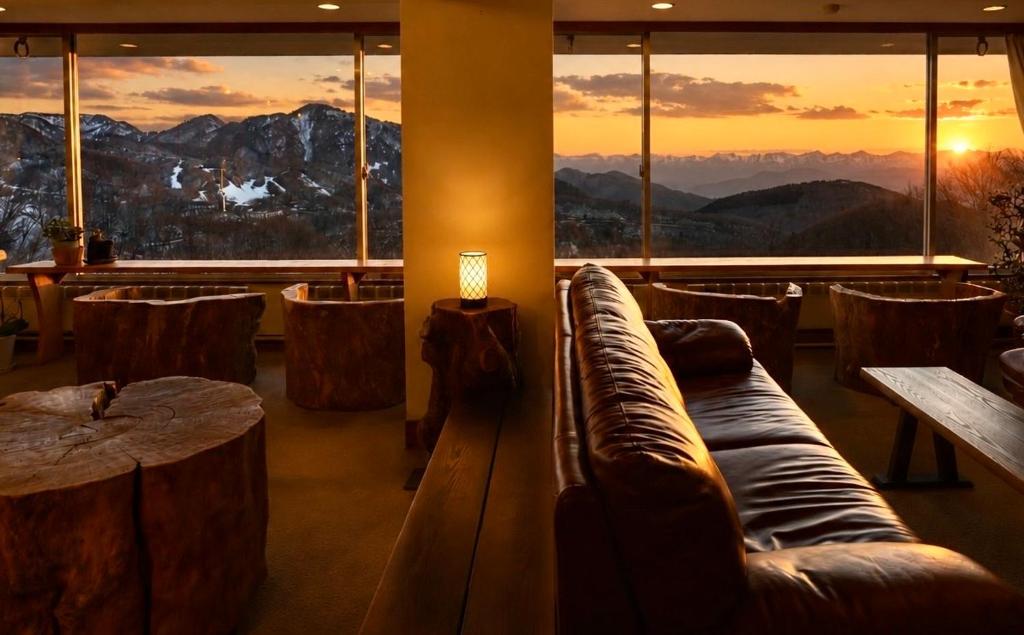 a room with a couch and a table and windows at Nishihoppo Onsen HOTEL in Yamanouchi