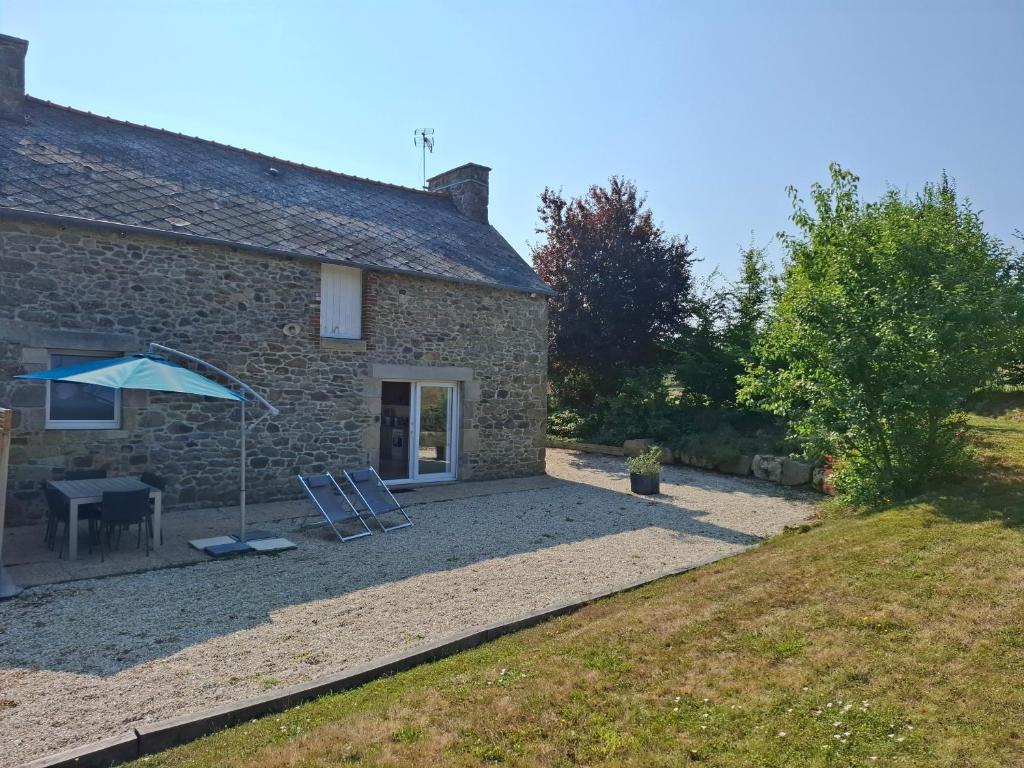 a stone cottage with a table and an umbrella at Logis du fresne in Saint-Lormel