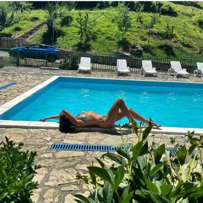 a woman laying on the ground next to a swimming pool at Etno Selo VRELO & Camping in Berane